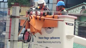 नेपाल विद्युत प्राधिकरणका प्राविधिकहरू सुरक्षा उपकरणसहित बकेट लिफ्ट प्रयोग गर्दै उच्च भोल्टेज विद्युत लाइनमा मर्मत कार्य गरिरहेको दृश्य।