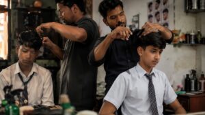 विद्यार्थीको कपाल काट्दै गरेको बार्बरको वास्तविक दृश्य, विद्यालय पोसाक लगाएका दुई विद्यार्थी बार्बर पसलमा कपाल काटाउँदै